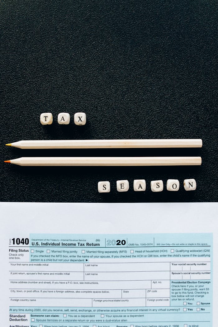 Creative composition featuring 1040 tax form, pencils, and letters spelling Tax Season on black background.
